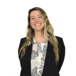 A portrait of a smiling Stephanie Mullins-Wiles, a white woman with long blonde hair, wearing a black jacket and white patterned blouse 