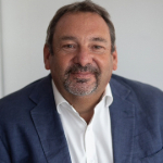 A colour portrait of Rod Cartwright. Rod is a white man with short brown hair and a beard who wears a blue jacket over a white collared shirt.