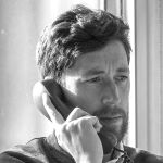 A black and white side portrait of Andy Silvester holding a phone to his ear. Andy is a white man with dark hair and beard 