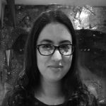 A portrait of a white woman with long dark hair with a dark top on and glasses