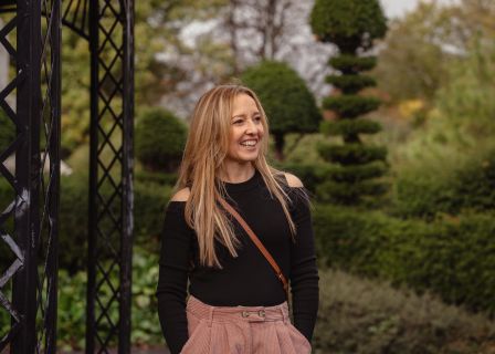 A photograph of Sharon Flaherty. It’s a late summer’s day, in a park in Cardiff surrounded by green trees.