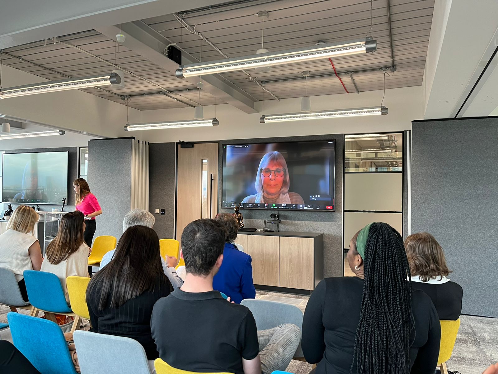 Dr Anne Gregory displayed on a large video screen in front of audience. Photograph shows the backs of the audience and Dr Anne's head and shoulders on screen.