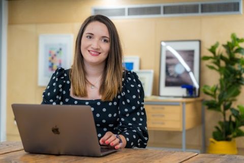 Shauna Madden sat a desk in front of a laptop and smiling.