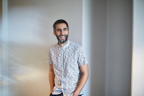 Keshi Bouri, a man with dark hair and beard, and wearing a floral patterned short-sleeved shirt looking to his left and smiling