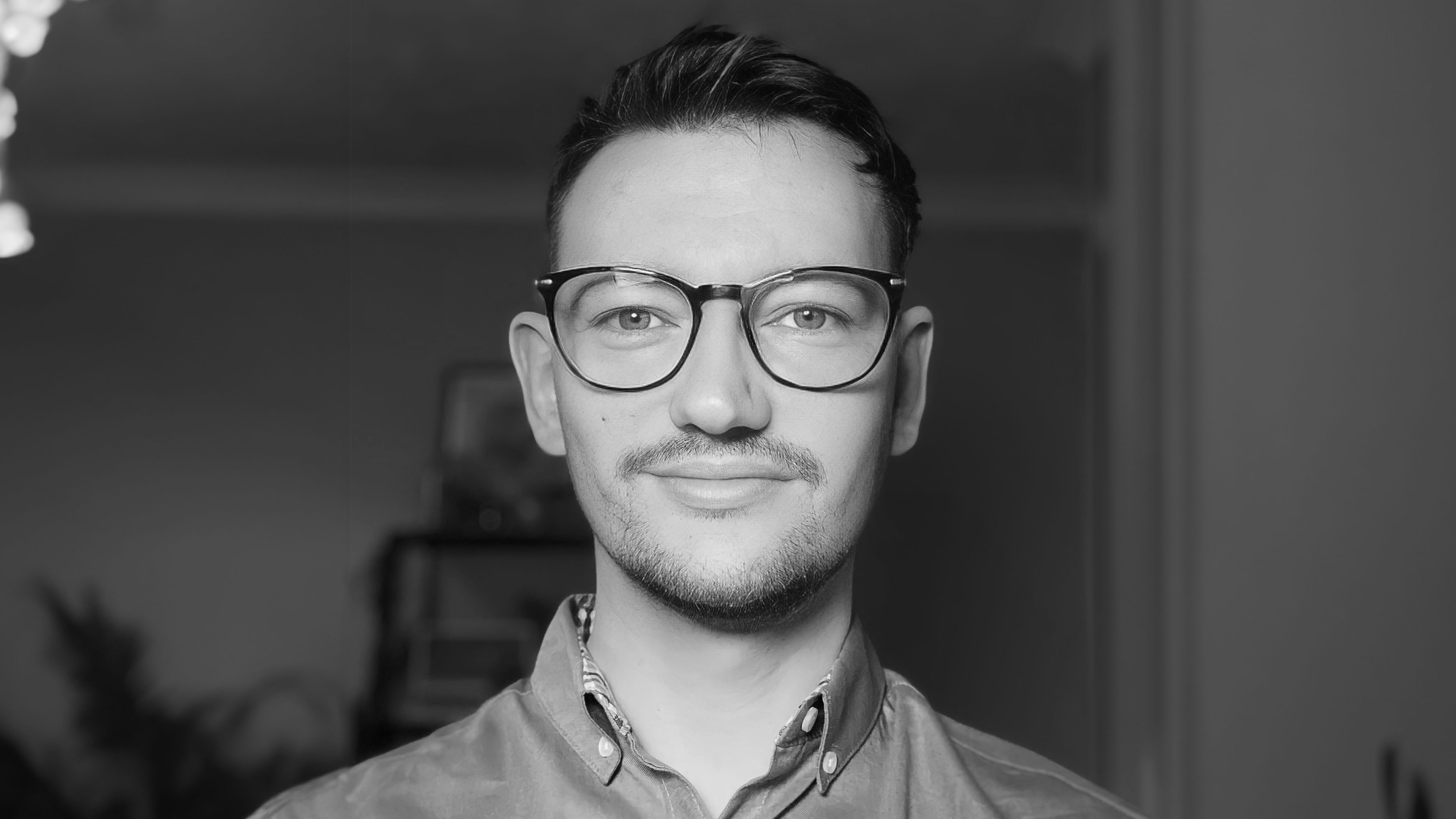 A black and white photo of James Sharp, a white man with dark hair, who wears glasses.