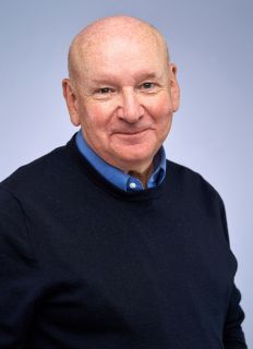 Chris Lewis, a white man, wearing a black jumper over a blue shirt.