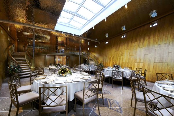 The ballroom on the Fingal featuring wood panel walls, large skylight in a copper ceiling, dual sweeping staircase and five large circular tables dresses for dinner