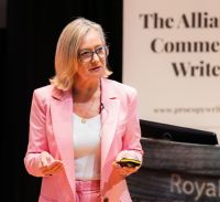 Lorraine Forrest-Turner, a white middle-aged woman with shoulder-length blond hair and glasses, wears a pink suite while giving a presentation.