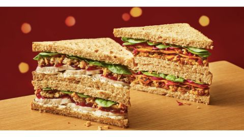 Two brown bread sandwiches cut diagonally with meat and salad fillings sat on a pale table with a red background with little circular lights