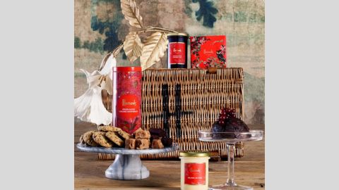 Harrods gift hamper basket surrounded by various items including a candle, Christmas pudding, biscuits red tins and box