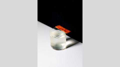 A translucent cocktail in a tumbler on a white surface, against a black background