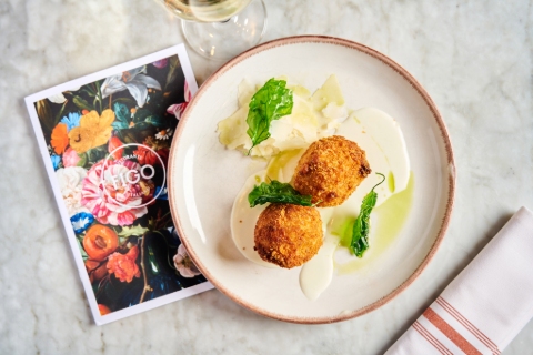 Two arancini balls with cheese, basil and drizzled in olive oil on a plate alongside a floral Fifo menu and napkin