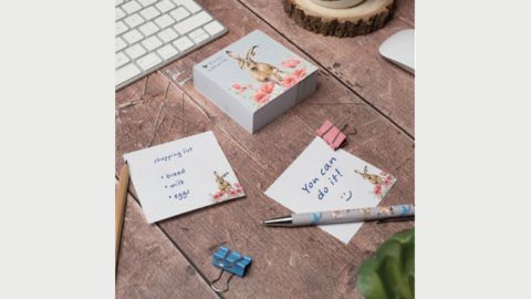 On a wooden desk various items of stationery are scattered including post-it notes, a pen, pencil and clips - there is the corner of a laptop keyboard on the picture