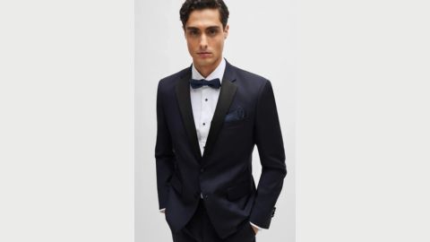 A male model with short dark hair wears a black dinner suit, white shirt and bow tie and looks direct at the camera