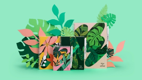 A set of notebooks in a variety of base colours including pink and black, emblazoned with bright coloured illustrations of leaves and flowers. Included in the design are cutouts of plant leaves. The background is green.