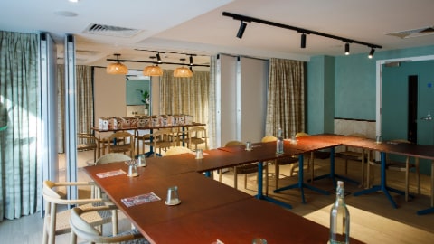 Dark wood tables set up in a square. Open curtains divide the room, with colourful bird boxes on another table in the adjoining room. 