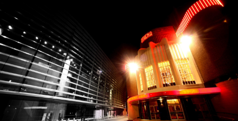 A night time shot of the colourful art decor exterior of the Athena, lit up in warm white and red lighting.