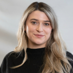 A colour portrait of Sarah Jardine. Sarah is a white woman with long blond hair wearing a black jumper.