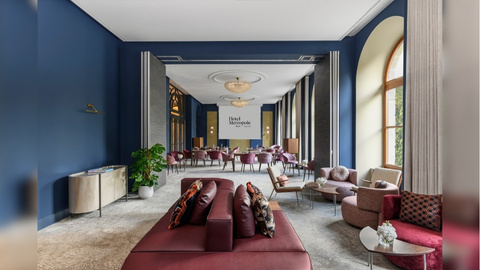 A wide angled shot of the Metropole Geneva lobby with blue walls, crean floor, and furnishings in maroon and cream.