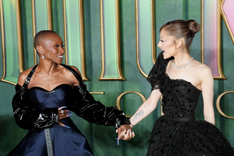 Cynthia Erivo and Ariana Grande both wearing black dresses holding hands and looking at each other