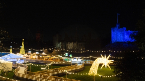 A winding path lit by golden lights and lit sculptures on a dark night. In the background is Cardiff Castle which is lit up in blue lights.
