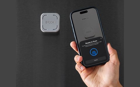 On a black background a hand hovers a mobile phone close to a small, grey plastic piece of equipment with the word Brick written on it.