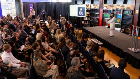 A photo taken from the side of the room of an audience watching comedian Jo Enright on stage.