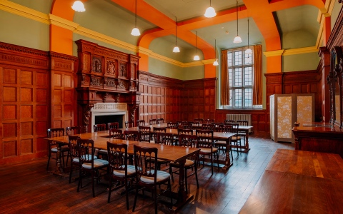 A room with wooden beams on the ceiling and wooden panelling on the walls set up for a meeting with chairs and tables