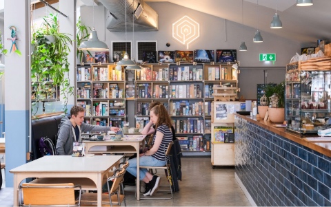 Three people sitting at a table playing a board game in front of shelves of other games