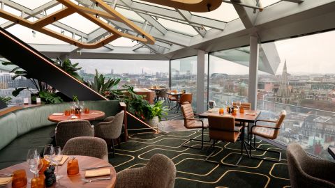 Floor to ceiling windows and a glass roof surround green and pink tables, chairs and curved sofas.