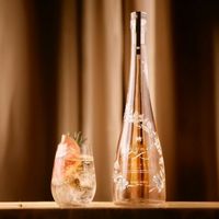 A slender pink gin bottle next to a gin glass.