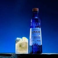 A blue bottle of tequila next to a glass.